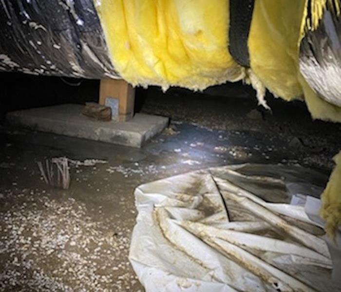 crawlspace with water and plastic covering the ground and an insulated pipe tied to the wood joist 